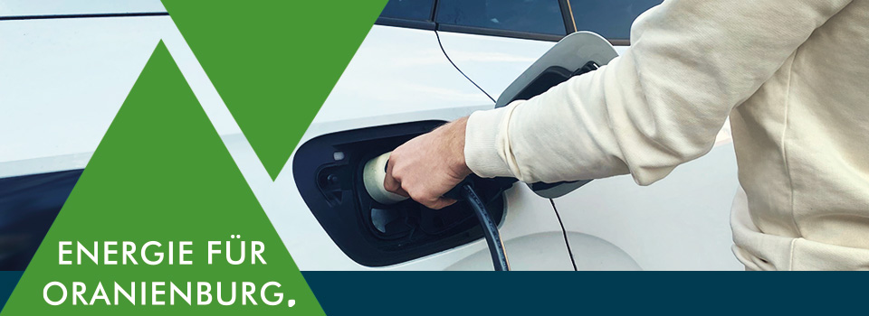 Grafik mit gr&uuml;nem Dreieck und dem Claim &sbquo;Energie f&uuml;r Oranienburg. &lsquo; vor einer Hand die ein E-Auto zum laden anschlie&szlig;t.
